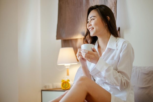 Mujer sosteniendo una taza de café en sus manosMujer tomando café en casa con amanecer en la ventana