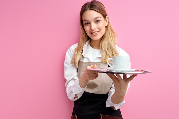 Mujer sosteniendo taza clásica blanca para café o té en bandeja aislada sobre fondo rosa studio.