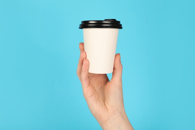 Mujer sosteniendo una taza de papel en un fondo azul claro Mockup para el diseño