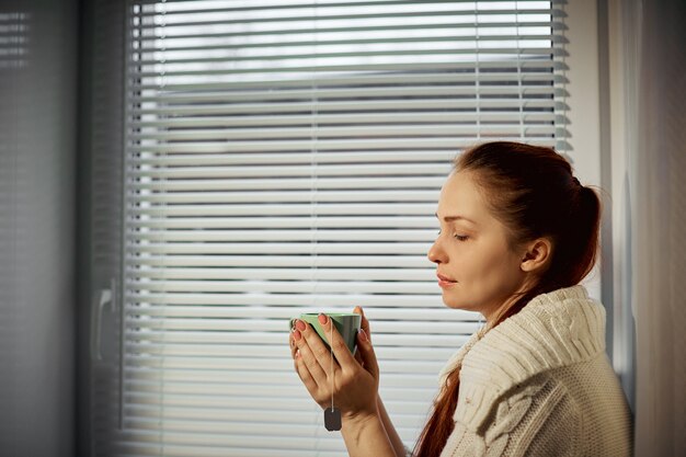 Mujer sosteniendo una taza de té y bebiendo sentados alrededor de la ventana.