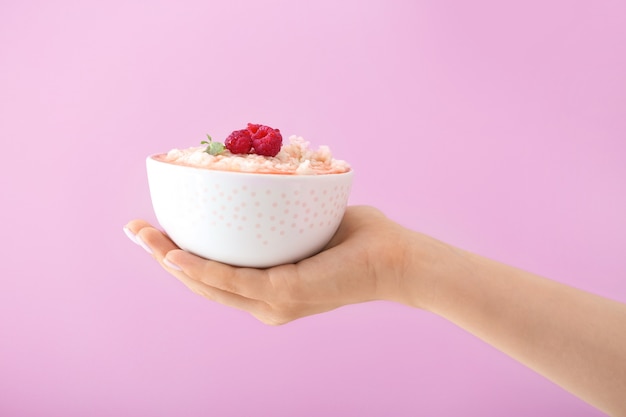 Mujer sosteniendo el tazón con delicioso arroz con leche sobre fondo de color