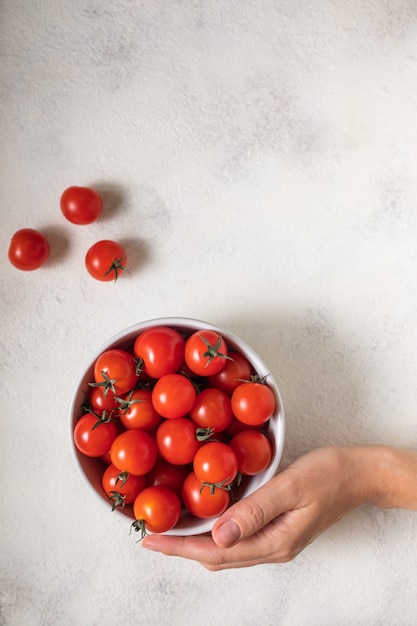 Mujer sosteniendo un tazón con tomates cherry maduros en la mesa, vista anterior