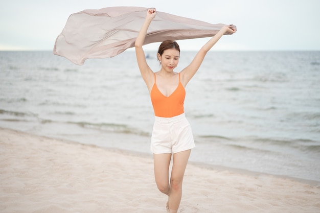 Mujer sosteniendo tela al viento en unas vacaciones en la playa. Viajar y saludable.