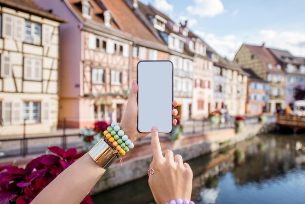 Mujer sosteniendo el teléfono en el fondo de edificios antiguos en la aldea de Colmar en Alsacia, en el noreste de Francia