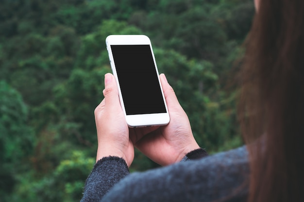 una mujer sosteniendo un teléfono inteligente blanco con pantalla en blanco en el exterior