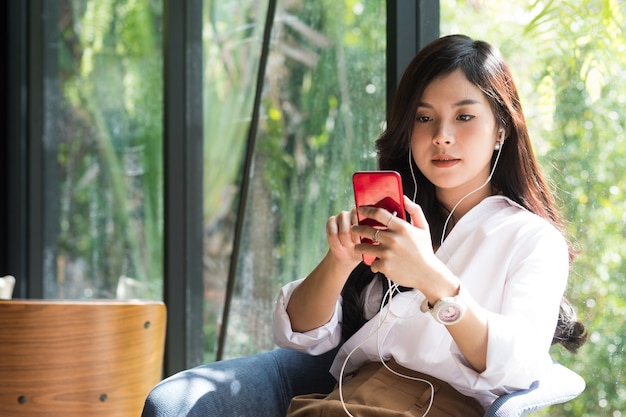 mujer sosteniendo un teléfono inteligente y escuchando música con auriculares