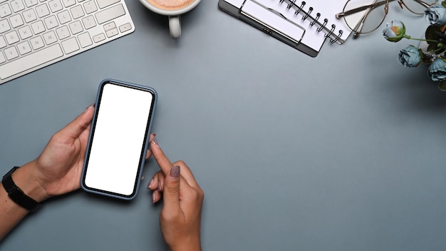 Mujer sosteniendo un teléfono inteligente con pantalla en blanco sobre fondo gris.