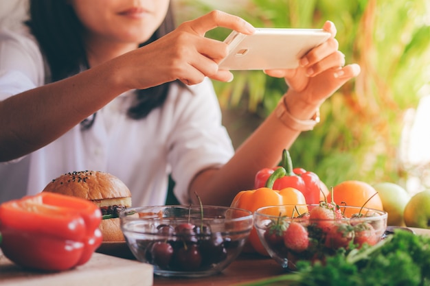 Foto mujer sosteniendo teléfono inteligente tomar una foto de comida en la mesa.