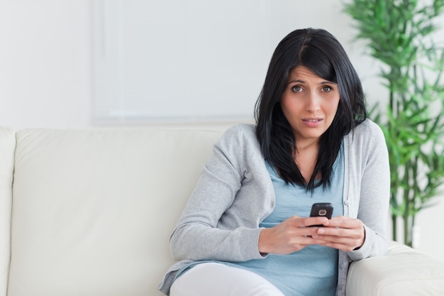 Mujer sosteniendo un teléfono mientras está sentado en un sofá