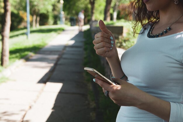 Mujer sosteniendo el teléfono y mostrando el pulgar hacia arriba en el parque