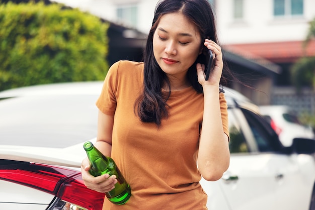 Mujer sosteniendo teléfono móvil y botella de cerveza en el coche. No beba y conduzca el concepto