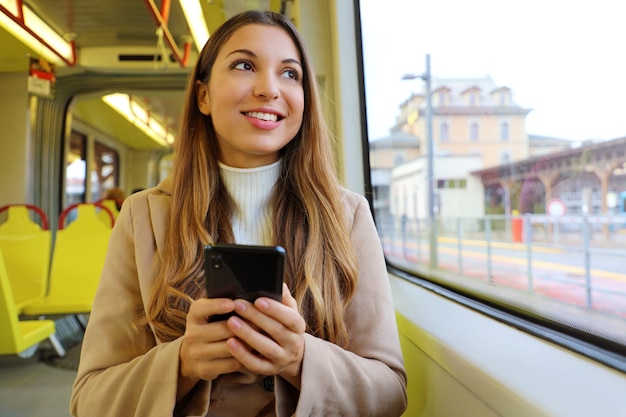 Mujer sosteniendo teléfono móvil mirando por la ventana del tranvía