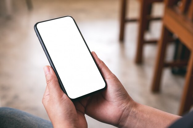 Una mujer sosteniendo teléfono móvil negro con pantalla en blanco mientras estaba sentado en la cafetería