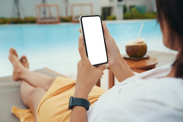 Mujer sosteniendo un teléfono de pantalla blanca relajándose en la piscina