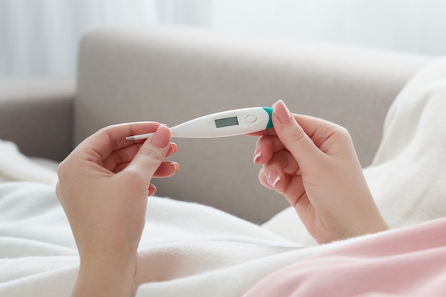 Mujer sosteniendo un termómetro digital. Concepto de fiebre, gripe, virus.