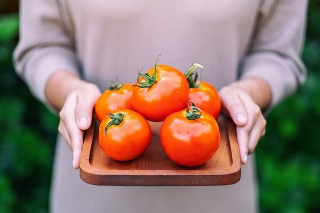 Foto una mujer sosteniendo un tomate fresco en una bandeja de madera