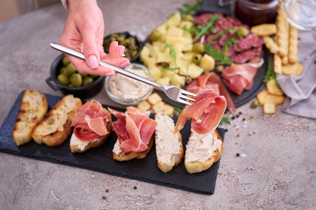 Mujer sosteniendo un trozo de jamón prosciutto en un tenedor de pie en la cocina doméstica