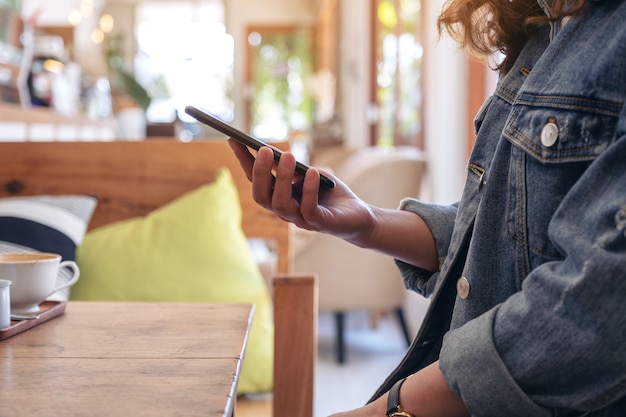 Mujer sosteniendo, usando y mirando el teléfono inteligente en el café