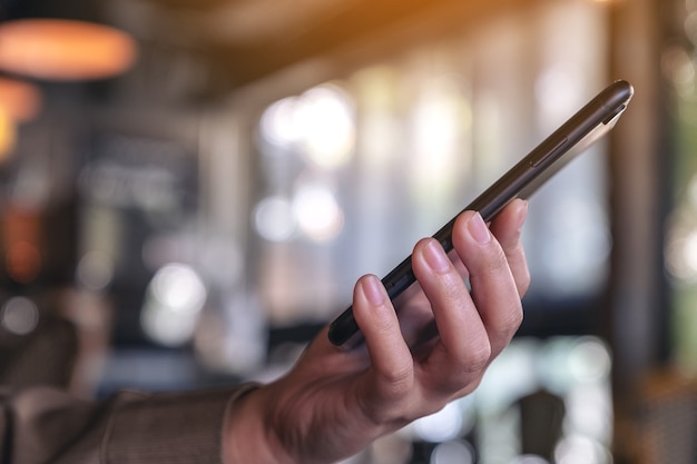 Una mujer sosteniendo y usando un teléfono inteligente negro en el café