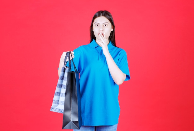 mujer sosteniendo varias bolsas de la compra azul y parece aterrorizada y confundida.