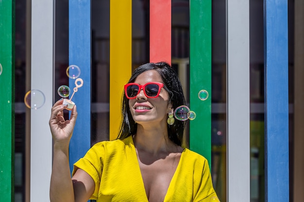 Foto mujer sosteniendo la varita de burbujas en un vestido amarillo y gafas de sol