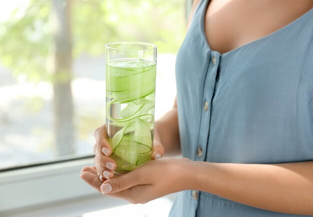 Foto mujer sosteniendo un vaso de agua de pepino fresco en casa