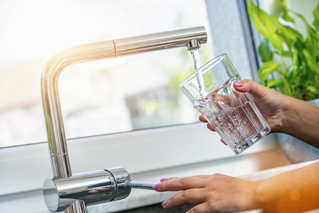 mujer sosteniendo un vaso en el grifo de agua y llenando agua