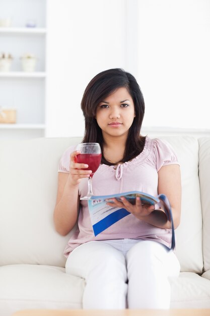 Mujer sosteniendo un vaso de vino rojo y una revista