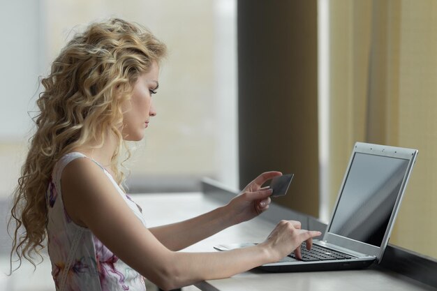 Mujer sosteniendo en un vestido una tarjeta de crédito y usando el teclado de la computadora para compras en línea.