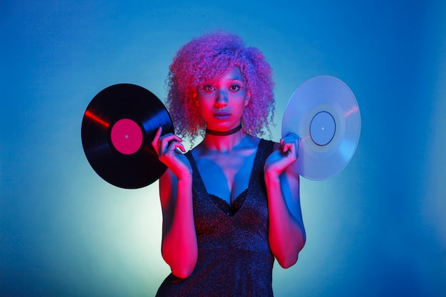 Mujer sosteniendo viejos vinilos de música en coloridas luces de neón