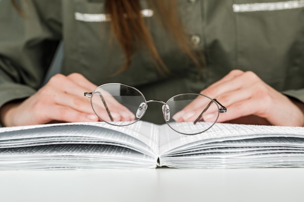 Una mujer sostiene anteojos con montura negra contra el fondo de un libro de texto abierto leyendo libros en Braille.