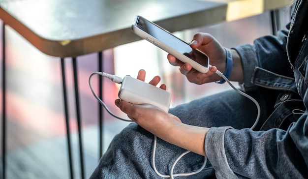 Una mujer sostiene un banco de energía y un teléfono en sus manos, carga el teléfono desde un banco de energía.