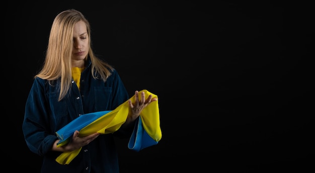 Mujer sostiene bandera azul y amarilla ucraniana sobre fondo negro copyspace crisis de guerra en blanco