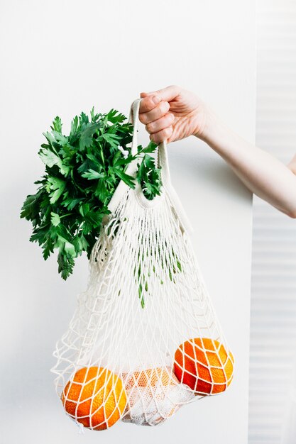 mujer sostiene una bolsa con alimentos verduras y frutas frescas