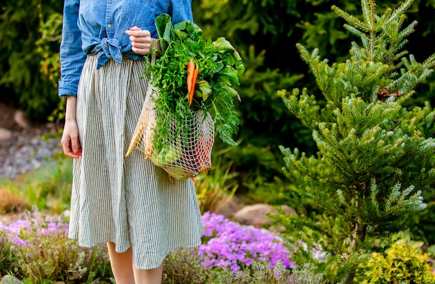 Mujer sostiene una bolsa de cadena con verduras en el jardín