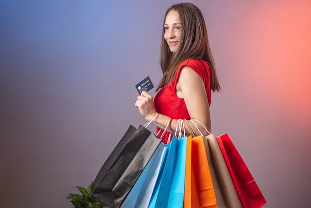 La mujer sostiene bolsas multicolores con compras y tarjeta de crédito