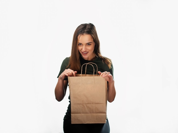 La mujer sostiene el bolso de compras en el fondo blanco. Bolsa de papel marrón claro en las manos. Fondo aislado.