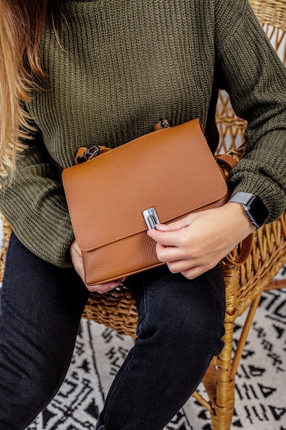 Una mujer sostiene un bolso de moda de cuero marrón en sus manos. Nueva colección de bolsos de mujer