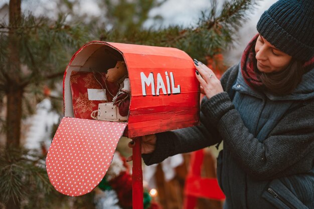 La mujer sostiene un buzón retro de lunares rojos con juguetes de regalos de navidad y una carta de felicitaci ...