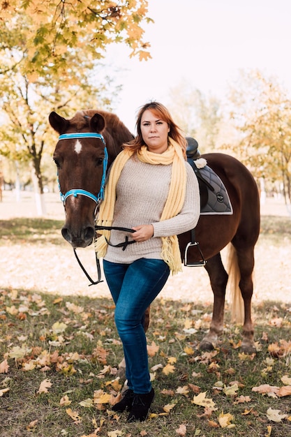 Foto mujer sostiene un caballo por las riendas a caballo en el bosque de otoño alquiler