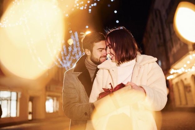 Mujer sostiene caja de regalo Feliz pareja joven celebrando el Año Nuevo al aire libre en la calle