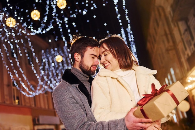 Mujer sostiene caja de regalo Feliz pareja joven celebrando el Año Nuevo al aire libre en la calle