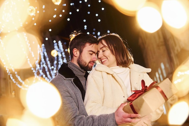 Mujer sostiene caja de regalo Feliz pareja joven celebrando el Año Nuevo al aire libre en la calle