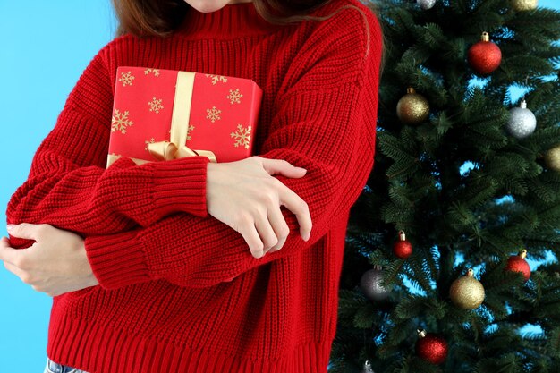 Mujer sostiene caja de regalo sobre fondo azul con árbol de Navidad