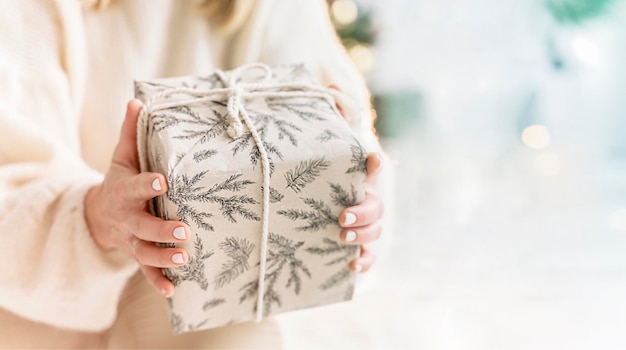 Una mujer sostiene una caja de regalo en sus manos en una noche de Navidad junto a un árbol de Navidad