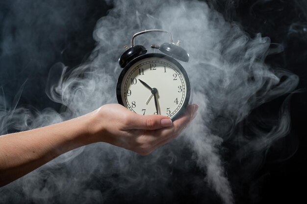 Una mujer sostiene un despertador en un estudio lleno de humo Niebla blanca envolvió un reloj mecánico retro redondo