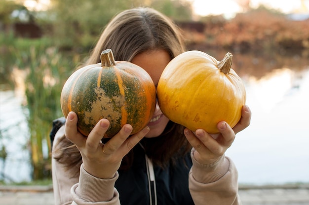 Foto una mujer sostiene dos calabazas en sus manos, cubriendo su rostro contra el fondo borroso de un estanque