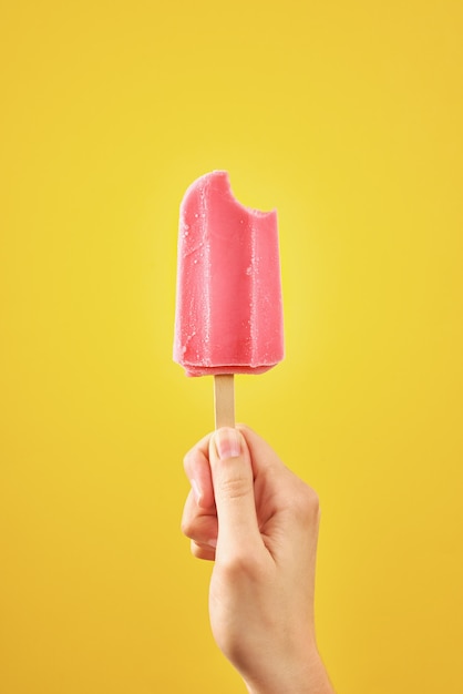 Mujer sostiene helado rojo mordido sobre fondo amarillo paleta de frutas congeladas de color