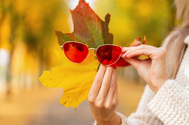 Foto la mujer sostiene hojas de otoño de colores brillantes con gafas de sol rojas en el parque de otoño idea creativa de otoño