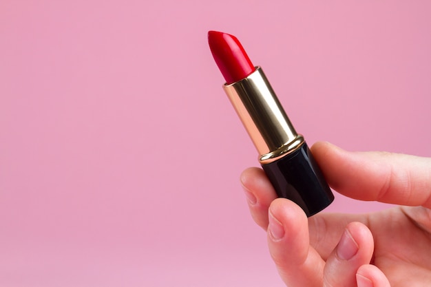 Una mujer sostiene el lápiz labial rojo en las manos. Cosmética femenina para maquillaje profesional. Copia espacio